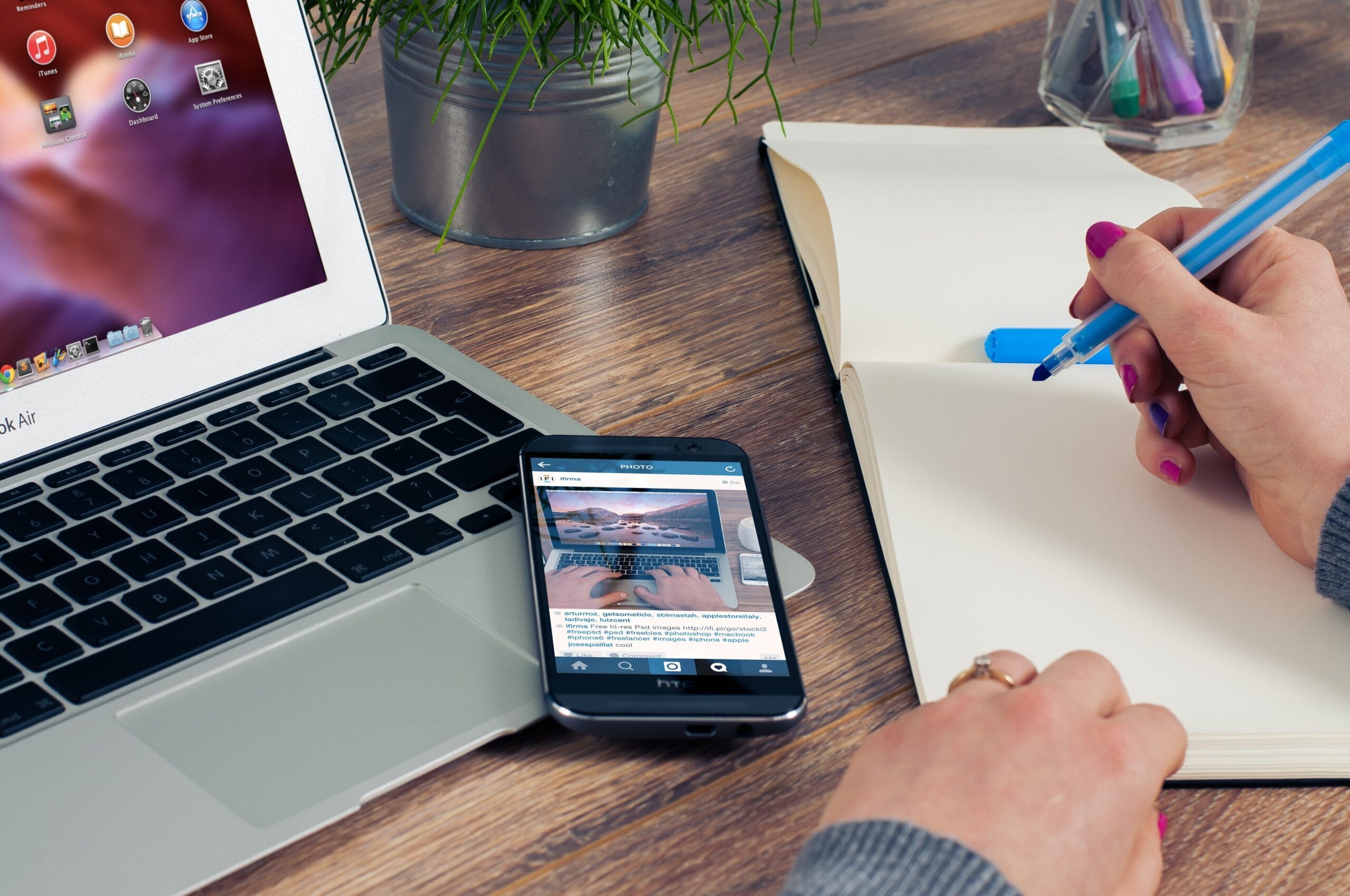 Virtual admin assistance services — A hand writing in a book in front of a laptop on a table. The writer is writing down the outline for his copywriting task.