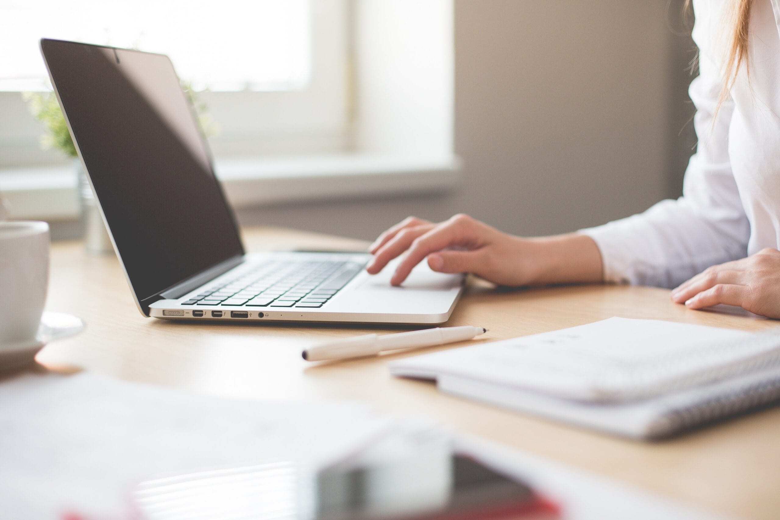 A laptop on the desk with the hands of a woman offering her virtual admin services from home.